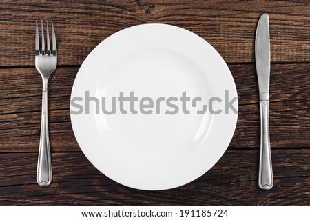 Empty plate, fork and table knife on old wooden background. Top view