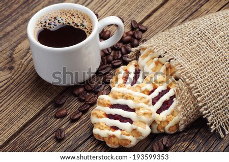 Sweet cookies with jam and icing and cup of coffee on vintage wooden table