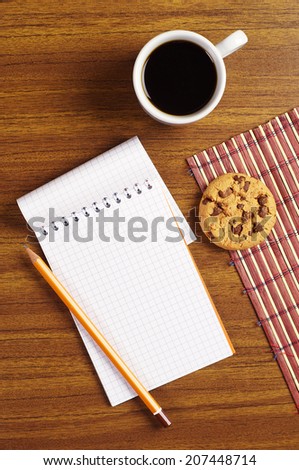 Cup of coffee with chocolate cookies and opened notepad on desk