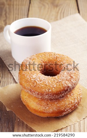 Donut with sugar and cup of hot coffee on wooden table