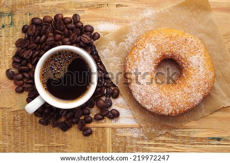 Donut with sugar and cup of hot coffee on wooden table. Top view
