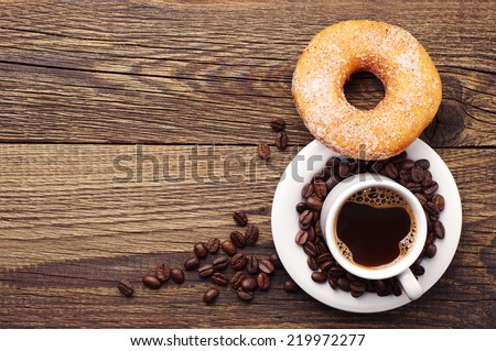 Donut with sugar and cup of hot coffee on old wooden table. Top view