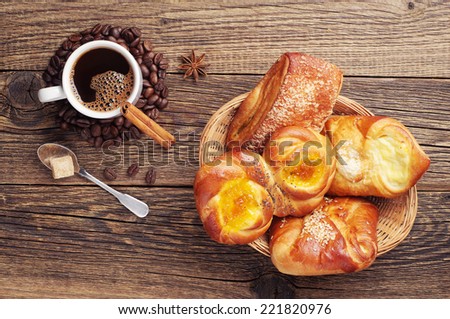 Sweet buns in wicker basket and coffee cup on old wooden table. Top view