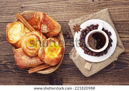 Coffee cup and sweet buns in wicker basket on old wooden table. Top view