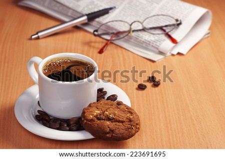 Cup of hot coffee with chocolate cookie and newspaper on table