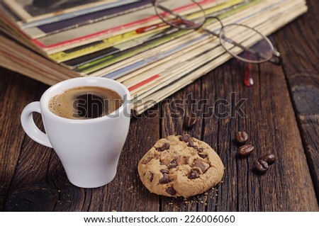 Cup of coffee with cookie and old magazines on wooden table