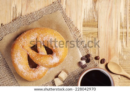 Sweet pretzel with sugar and cup of coffee on wooden table. Top view