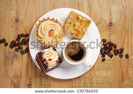 Three cakes and coffee cup in white plate on old wooden table. Top view