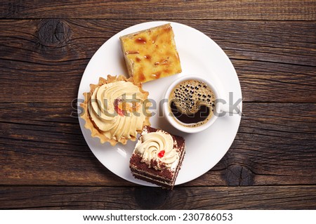 Plate with cakes and coffee cup on dark wooden table. Top view