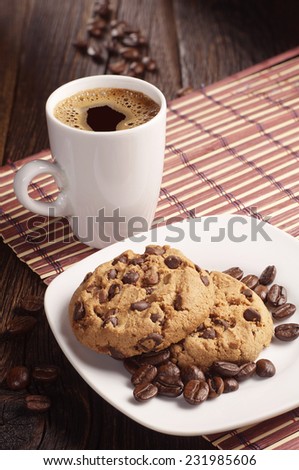 Chocolate cookies in plate and cup of hot coffee on bamboo napkin