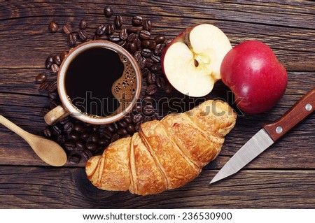 Coffee, croissant and two halves of an apple on a dark wooden table, top view
