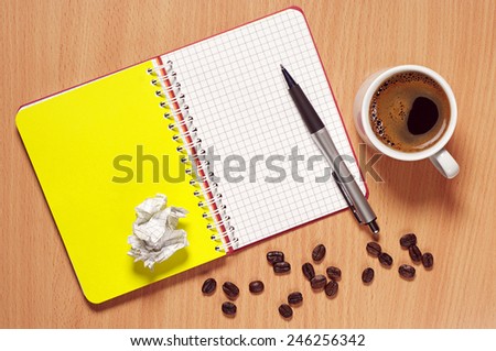 Opened notebook, pen and cup of hot coffee on desk, top view