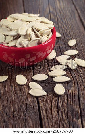 Pumpkin seeds in red bowl and scattered on rustic wooden table