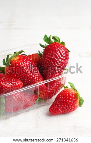 Ripe strawberries in plastic packing on old white table