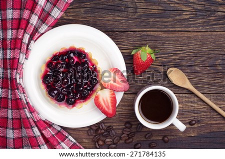 Cake with black currants, strawberry and coffee cup on dark wooden table, top view