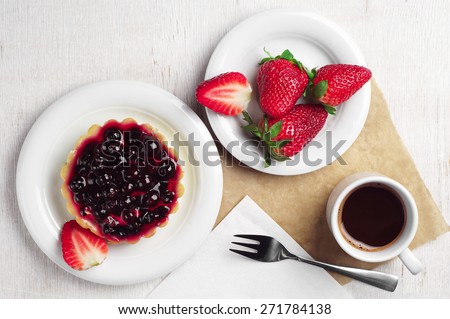 Cake with black currants, strawberry and coffee cup on table, top view