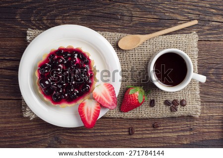Cup of coffee, cake with black currants and strawberry on wooden table, top view