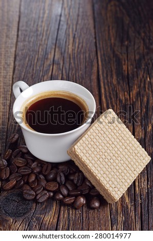 Cup of hot coffee and delicious wafers with chocolate on dark wooden table