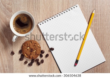 Cup of hot coffee with chocolate cookie and notepad on desk from above