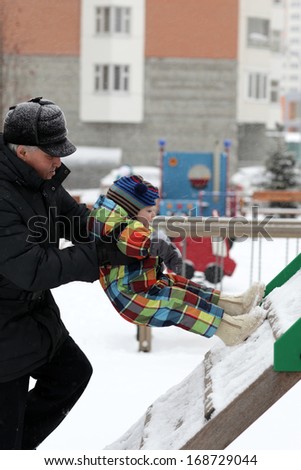 Grandfather helping his grandson to climb the slide in winter