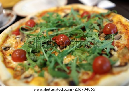 Pizza with arugula and cherry tomatoes in the cafe