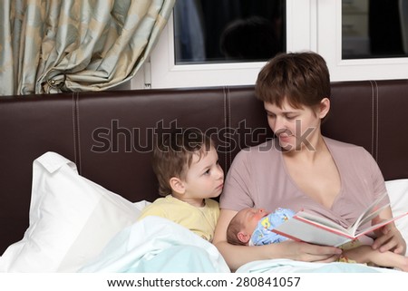 Mother reading book for her sons in the bed at home