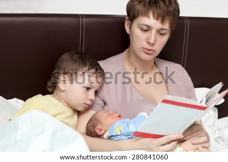 Mother reading book for her sons in the bed