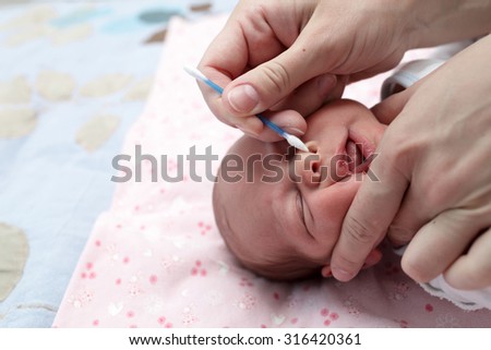 Mother cleaning baby boy nose with cotton swab