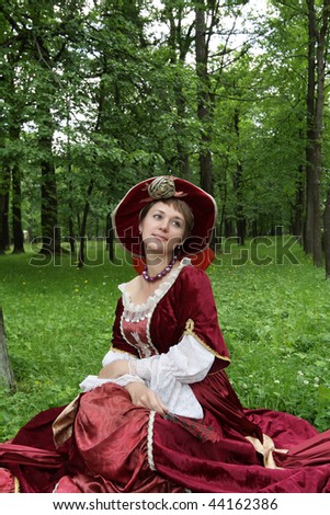 The woman poses in red victorian dress in park