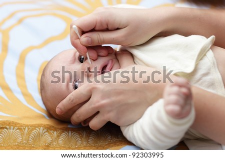 A mother cleaning baby nose by cotton swab after bath at home