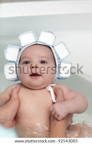 The happy baby in bath in a swim cap at home