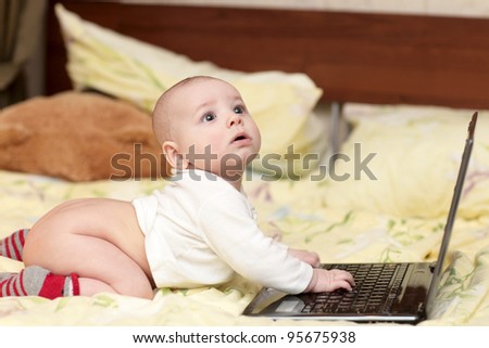 The surprised baby with laptop on a bed at home
