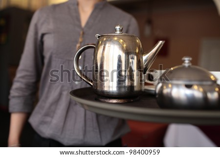 A waitress holding a tray with metallic teapot