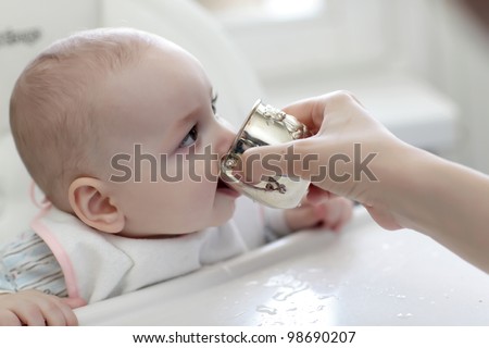 The baby boy drinking water from silver cup at home