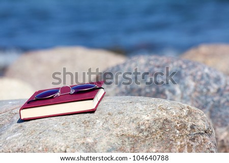 Closed Book with dark tinted sun glasses lies on a rock on the beach