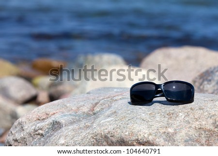 Sunglasses with dark tinted glasses lies on a rock on the coast