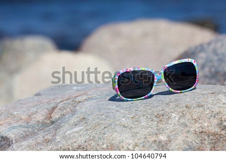Sunglasses with colorful floral eyeglass frame lies on a rock on the coast