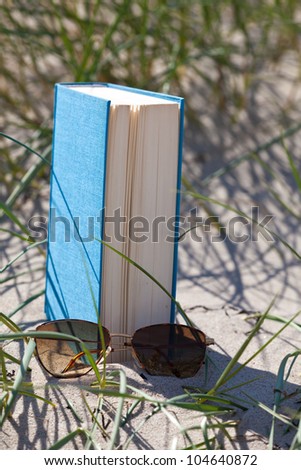A book with a sun glass lying in the sand in a dune