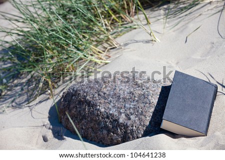A closed book lies in the sand at a stone