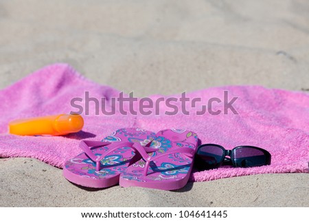 With flip-flops, beach towel, sun cream and sunglasses on the beach