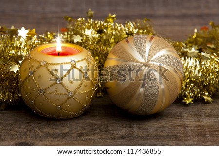 Candle in the golden candle holder and golden Christmas tree ball with golden garland on wooden background