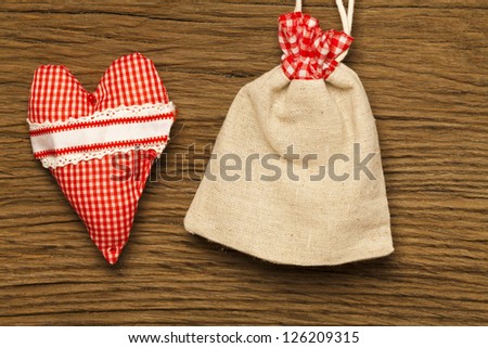 A red and white checked fabric cushion and a small jute bag before wood background