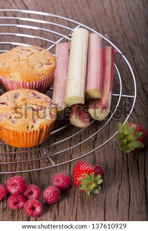 Two whole strawberry rhubarb and raspberry muffins with fresh fruit on a cake wire rack
