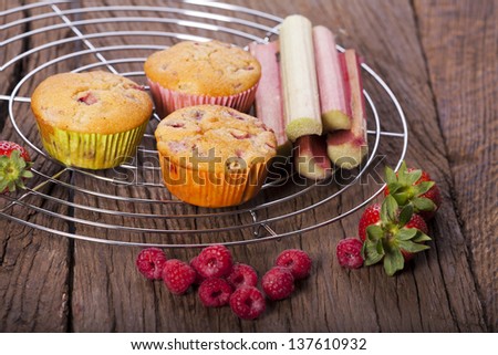 Several whole strawberry rhubarb and raspberry muffins with fresh fruit on a cake wire rack