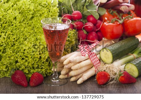 Fresh vegetables with asparagus and strawberries on a wooden background and a glass of rose wine