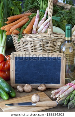 Fresh market vegetables with mushrooms, asparagus, bottle of wine and a blank slate as a menu card on a rustic wooden background