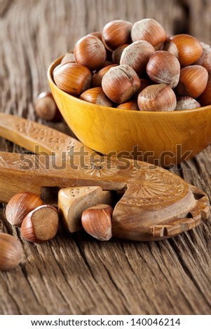 Hazelnuts in a wooden bowl with a wooden nutcracker on a rustic wooden background