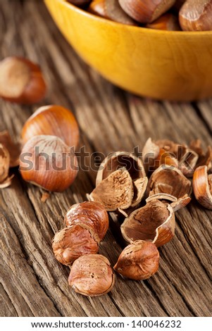Hazelnut kernels and shells and a bowl of hazelnuts in the background on a rustic wooden background