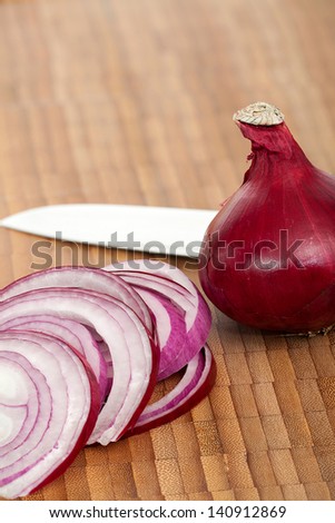 A whole red onion and onion rings with a knife on a cutting board
