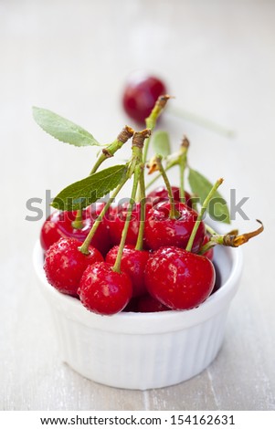 Some Freshly picked ripe cherries with stem and leaves in a bowl, in the background, blurred a cherry